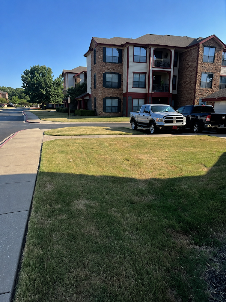 Residential apartment community with well-maintained lawns, sidewalks, trees, and landscaped grounds